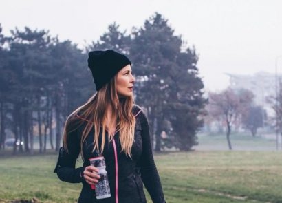 Woman in fitness gear and woolly hat walking across a field