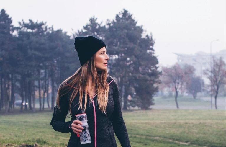 Woman in fitness gear and woolly hat walking across a field