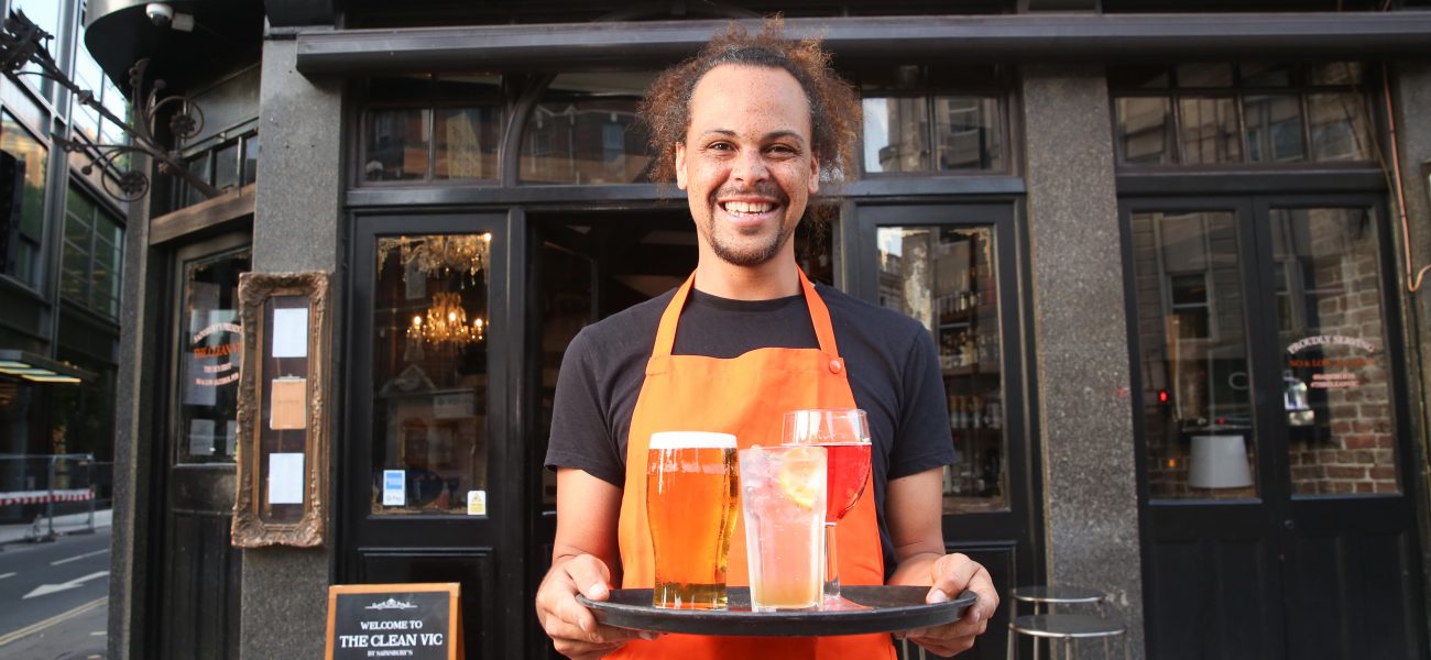 Man holding a tray of non-alcoholic drinks outside pub