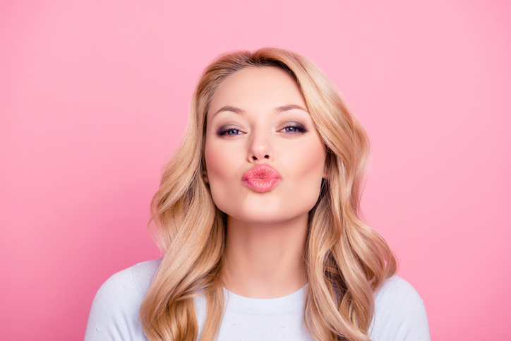 Young woman pouting at the camera in front of pink background