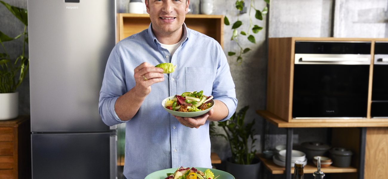 Jamie Oliver holding a freshly made dish that looks too delicious to eat