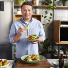 Jamie Oliver holding a freshly made dish that looks too delicious to eat