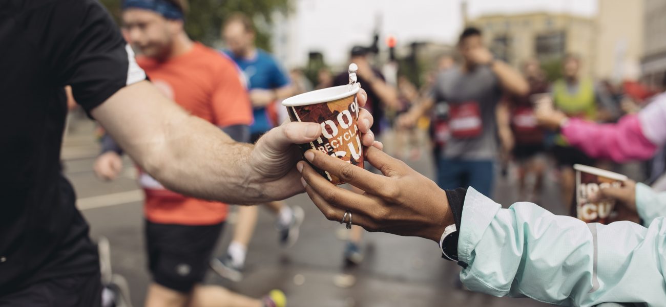 Runner being handed a cardboard cup of water on race