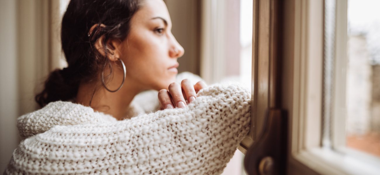 Millennial woman looking out the window feeling lonely