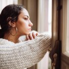 Millennial woman looking out the window feeling lonely