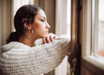 Millennial woman looking out the window feeling lonely