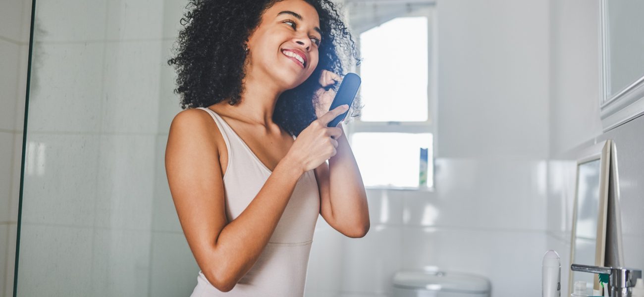 Woman brushing her hair inside her bathroom, after learning not to make these hair mistakes