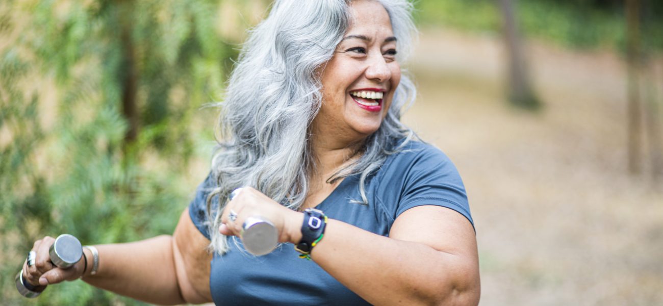 Happy older woman smiling and using weights outdoors