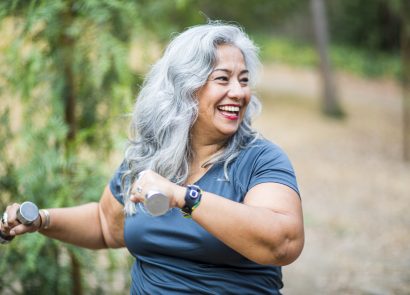 Happy older woman smiling and using weights outdoors