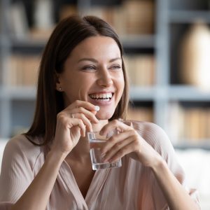 Woman smiling, holding pill and glass of water, after beating bloating