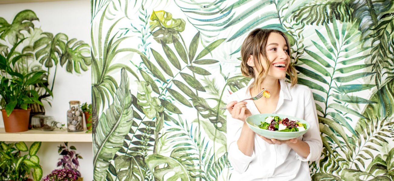 Woman eating vegan food in front of forest-themed wallpaper