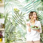 Woman eating vegan food in front of forest-themed wallpaper