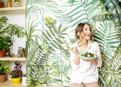Woman eating vegan food in front of forest-themed wallpaper