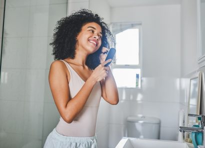 Woman brushing her hair inside her bathroom, after learning not to make these hair mistakes
