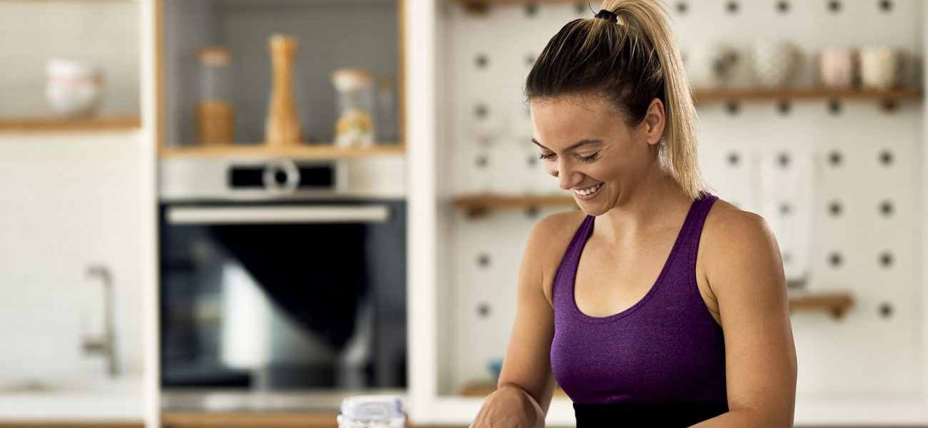 Happy athletic woman cutting fruit while preparing healthy meal in the kitchen.