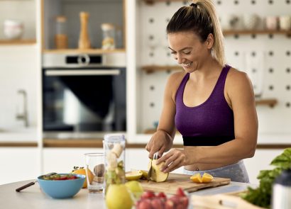 Happy athletic woman cutting fruit while preparing healthy meal in the kitchen.