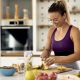 Happy athletic woman cutting fruit while preparing healthy meal in the kitchen.