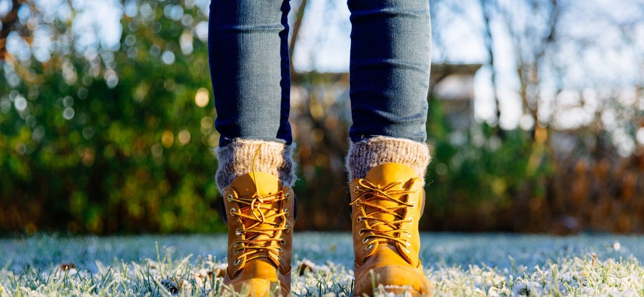 person's feet with winter boots and sock standing on frosty grass