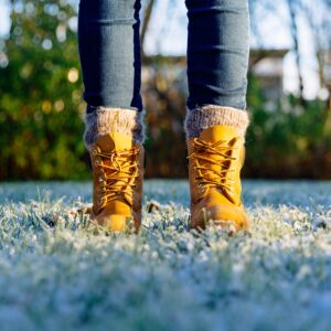 person's feet with winter boots and sock standing on frosty grass