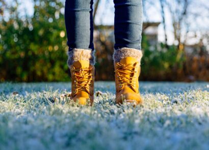 person's feet with winter boots and sock standing on frosty grass