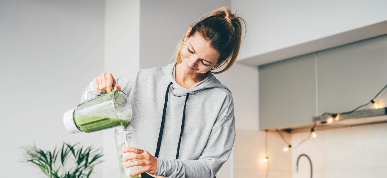 woman in loungewear making a healthy green smoothie in a modern kitchen
