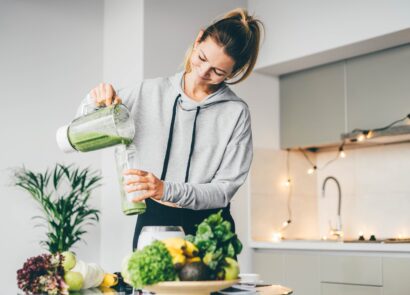 woman in loungewear making a healthy green smoothie in a modern kitchen