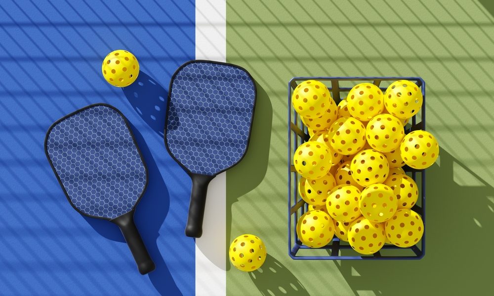 Two Pickleball paddles and basket of balls on court under