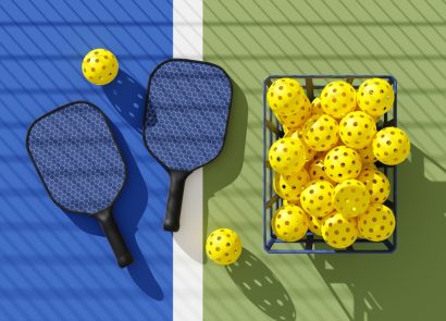 Two Pickleball paddles and basket of balls on court under