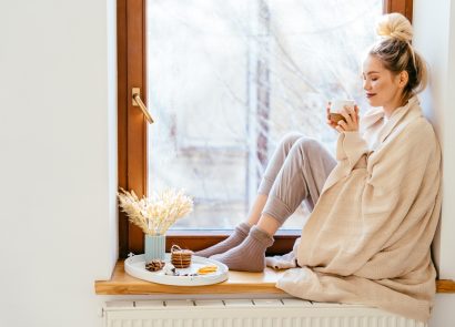 Happy blond woman with bunch hairstyle warming and cover knitted plaid enjoying in her coffee time by the window in cold winter day