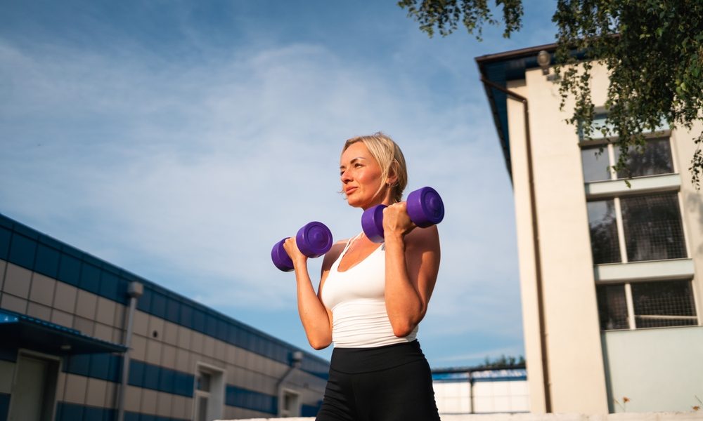 Beautiful blonde middle age woman doing weights exercises with dumbbells outdoors