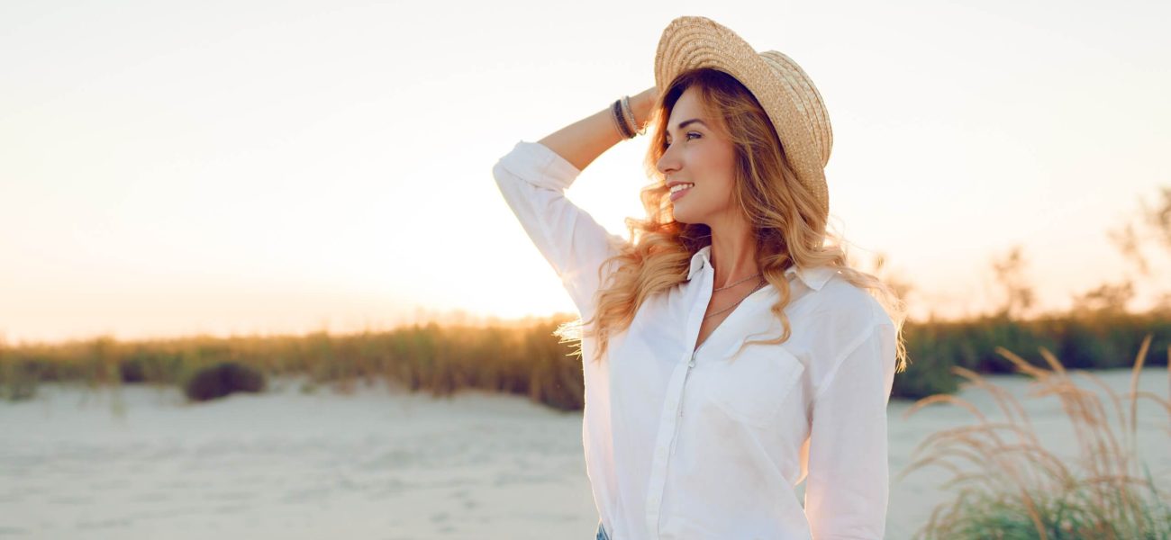 A woman wearing a hat standing beside a river
