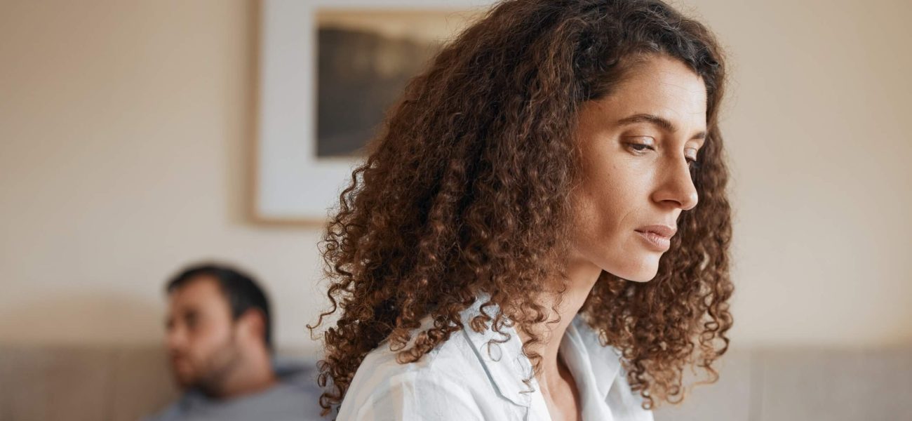 A woman looking concerned as her partner looks away in the background