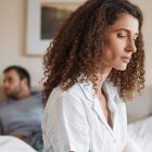 A woman looking concerned as her partner looks away in the background