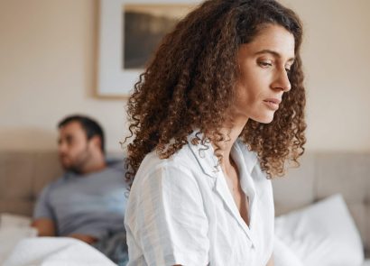 A woman looking concerned as her partner looks away in the background