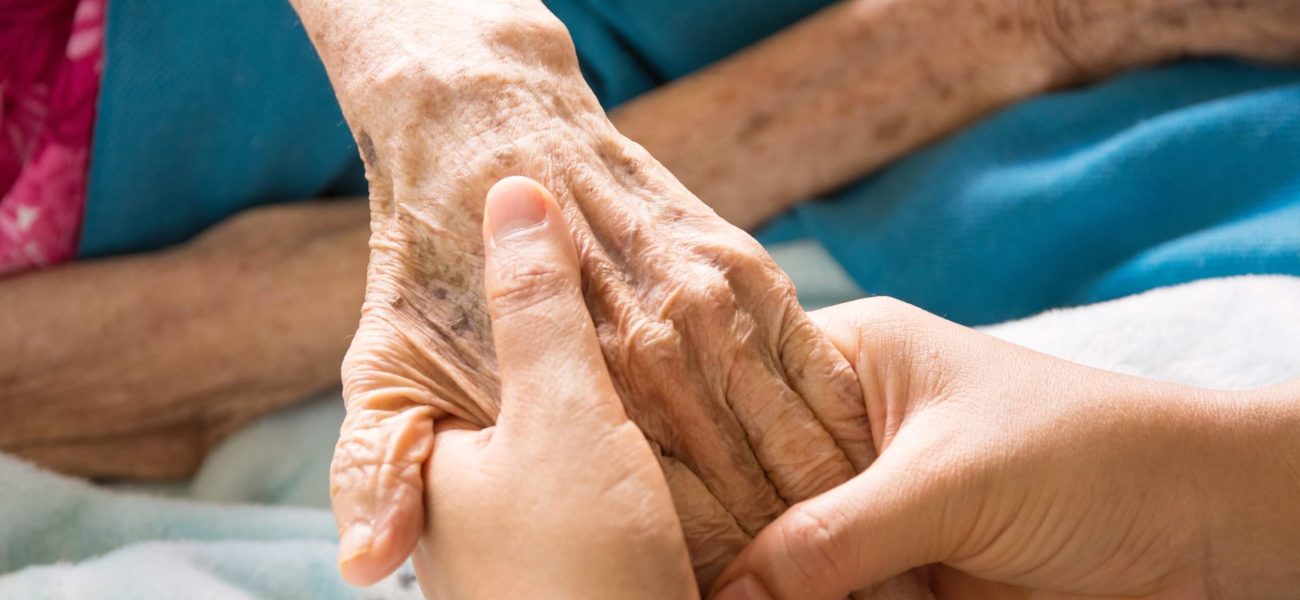 Two hands holding an elderly person's hand