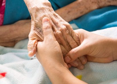Two hands holding an elderly person's hand