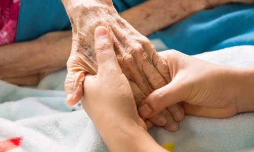 Two hands holding an elderly person's hand