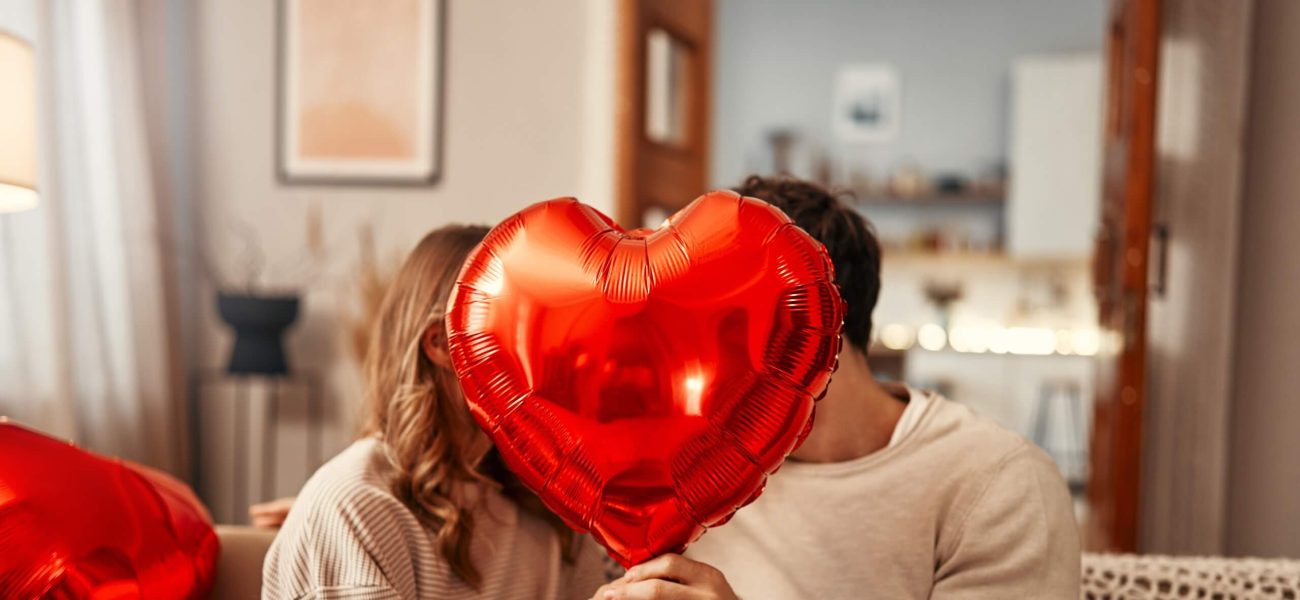A man woman sitting in a house holding a heart-shaped balloon