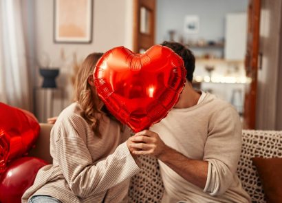 A man woman sitting in a house holding a heart-shaped balloon