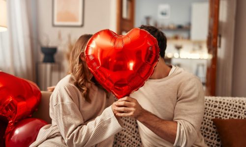 A man woman sitting in a house holding a heart-shaped balloon