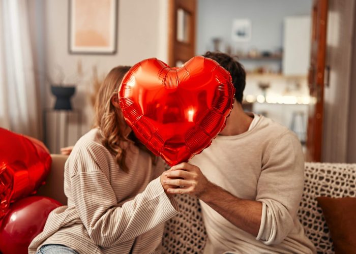 A man woman sitting in a house holding a heart-shaped balloon