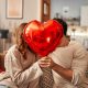 A man woman sitting in a house holding a heart-shaped balloon