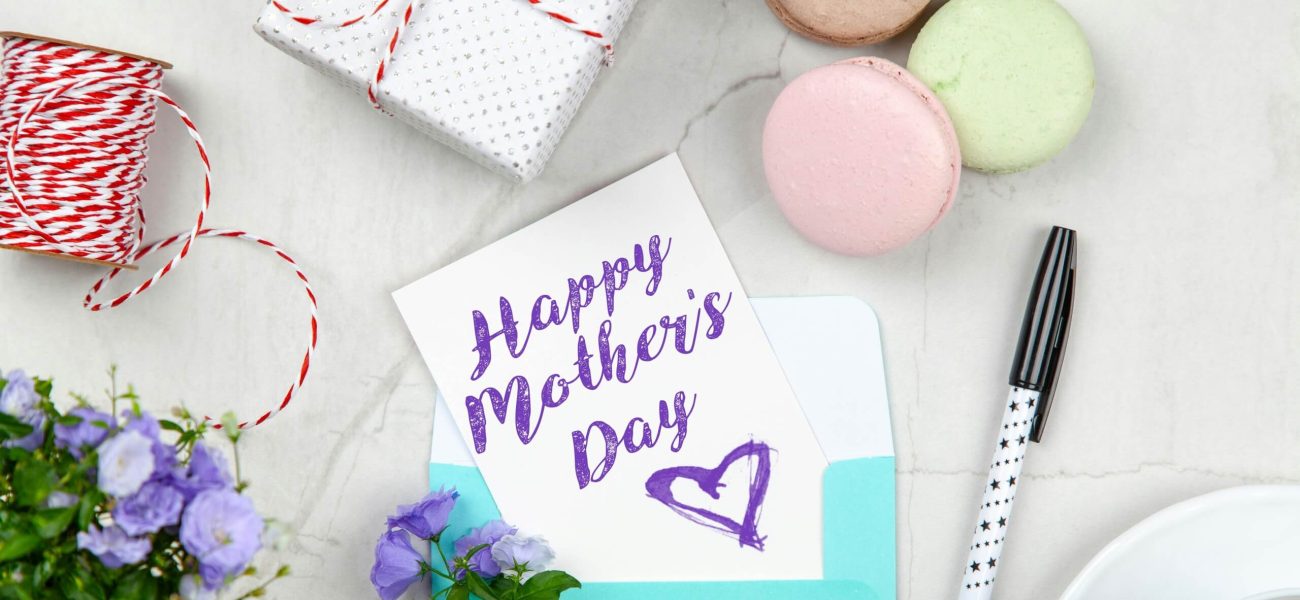 A handwritten Mother's Day card on a table next to a pen and a cup of coffee