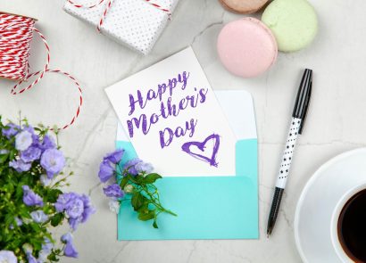 A handwritten Mother's Day card on a table next to a pen and a cup of coffee