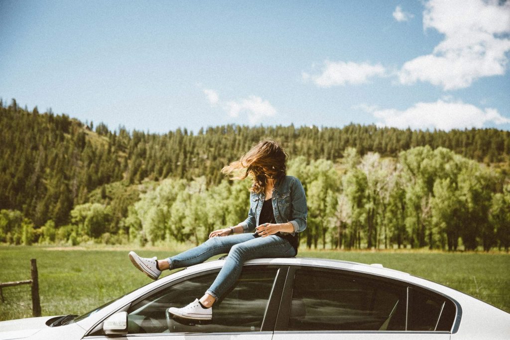 A woman sitting on the roof of a car in the countryside