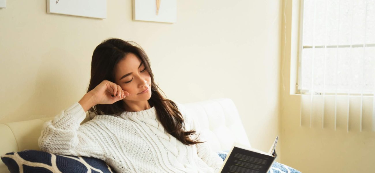 A woman reading a book on a sofa at home
