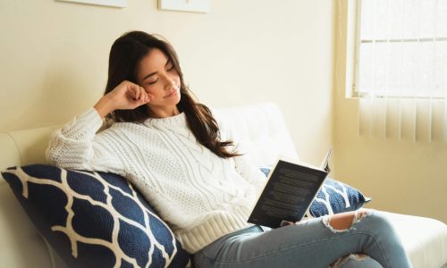 A woman reading a book on a sofa at home