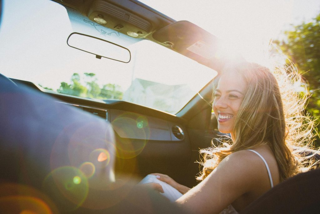 A woman, driving as a passenger in a convertible car