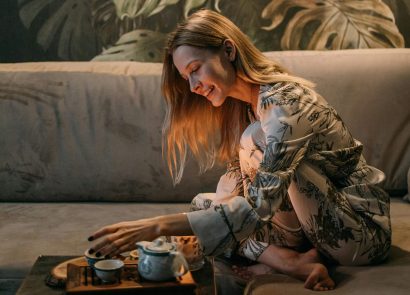 A woman sitting on a sofa in her pyjamas preparing a cup of tea