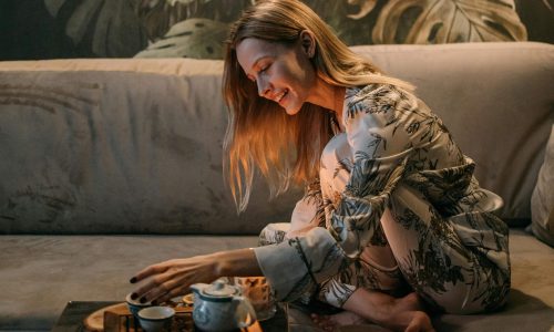 A woman sitting on a sofa in her pyjamas preparing a cup of tea